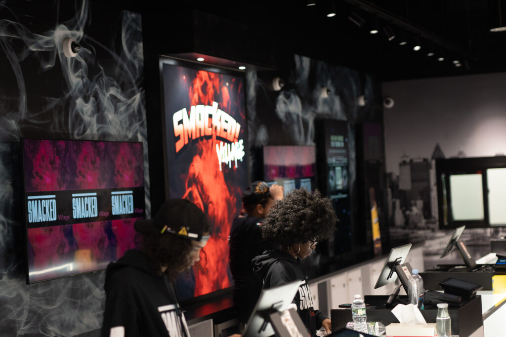 Budtenders at the Smacked Village counter in West Village NYC, assisting customers beneath branded displays.