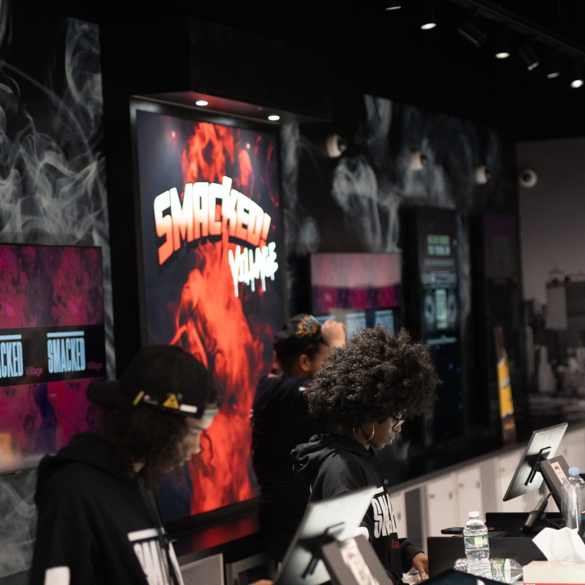 Budtenders at the Smacked Village counter in West Village NYC, assisting customers beneath branded displays.